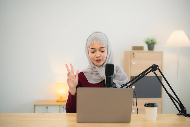 Müslüman İslam serbest girişimci kadın tesettür takıyor ve konferans sırasında konuşuyor, mikrofon ve dizüstü bilgisayarla çalışıyor ve merkez ofisteki masa başında çalışıyor. İş konferansı teknolojisi. - Fotoğraf, Görsel