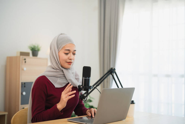 Müslüman İslam serbest girişimci kadın tesettür takıyor ve konferans sırasında konuşuyor, mikrofon ve dizüstü bilgisayarla çalışıyor ve merkez ofisteki masa başında çalışıyor. İş konferansı teknolojisi. - Fotoğraf, Görsel