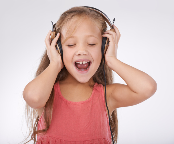 Lány gyerek, zene és éneklés fejhallgatóval stúdióban audio, előfizetés és streaming multimédia fehér háttérrel. Boldog gyermek, kiabálás és hallgatás podcast, hallás hang és rádió. - Fotó, kép
