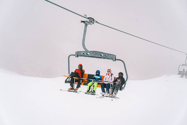 Sciatori in tute da sci colorate sugli sci con bastoncini cavalcano su una seggiovia a quattro posti lungo la pista. Foto di alta qualità - Foto, immagini