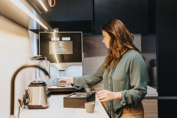 Υπέροχο κορίτσι ετοιμάζεται καφέ ή τσάι σε δροσερή κουζίνα στο γραφείο, νωρίς το πρωί πριν από τη δουλειά. - Φωτογραφία, εικόνα