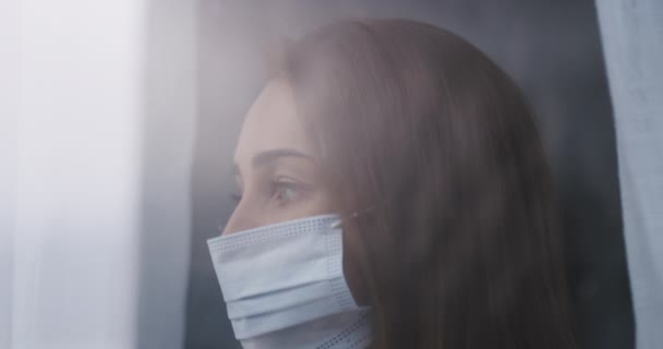 Face mask, thinking and woman by window in home for reflection, remember and wondering. Quarantine, healthcare and closeup of person by glass with protection for disease, sickness and epidemic safety. - Footage, Video