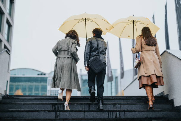 Amigos compartilhando guarda-chuvas subindo escadas na cidade em um dia chuvoso. - Foto, Imagem