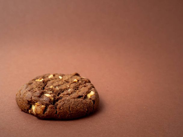 Σοκολατένια, πλούσια μπισκότα με αντιθέσεις σε μάρκες λευκής σοκολάτας σε καφέ φόντο. Cookies με λευκή σοκολάτα close-up. - Φωτογραφία, εικόνα