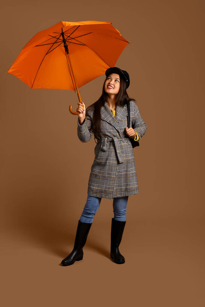 Beautiful young Asian woman with umbrella on brown background - Photo, Image