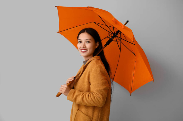Красивая молодая азиатка с зонтиком на сером фоне - Фото, изображение