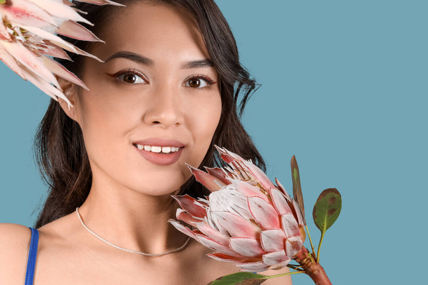Pretty young Asian woman with beautiful protea flowers on blue background, closeup - Photo, Image