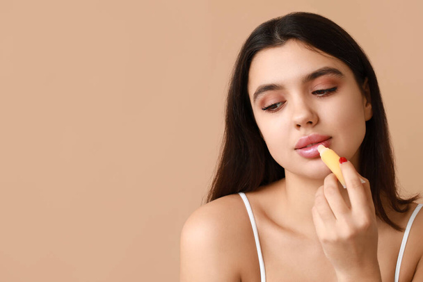Όμορφη νεαρή γυναίκα εφαρμογή lip balm στο φόντο χρώμα - Φωτογραφία, εικόνα
