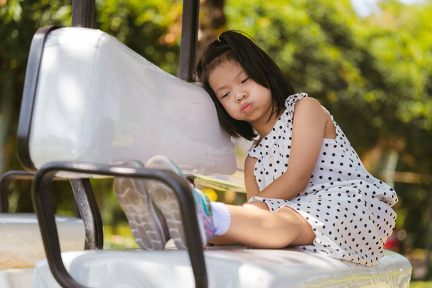 Jeune fille âgée de 6 ans rêvant dans le parc, Thoughtful Kid repose sa joue sur le coussin du dossier alors qu'elle est assise dans une voiturette de golf, apparemment perdue dans des rêveries au milieu de la tranquillité d'un parc ensoleillé. - Photo, image