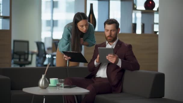 Ciddi iş ortakları büyük modern ofis içinde tablet şirket işlerini tartışıyor. Odaklanmış profesyonel avukat rahat koltukta bilgisayar ekranına bakıyor. Başarılı pazarlama çifti kavramı - Video, Çekim
