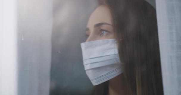 Face mask, thinking and woman by window in home for reflection, sadness and wondering. Quarantine, healthcare and portrait of person by glass in protection for pandemic, sick or epidemic safety. - Footage, Video
