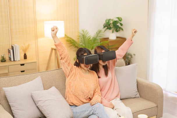 Estilo de vida em casa conceito, casal lésbico LGBT em óculos VR para jogar e fazer gesto de vitória. - Foto, Imagem