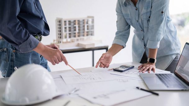 Zwei Ingenieure Architekt zeigt auf Entwurf der Skizze Innenarchitektur Gebäude zur Diskussion technische für Bauplan und Baumodell während der Zusammenarbeit am Arbeitsplatz. - Foto, Bild