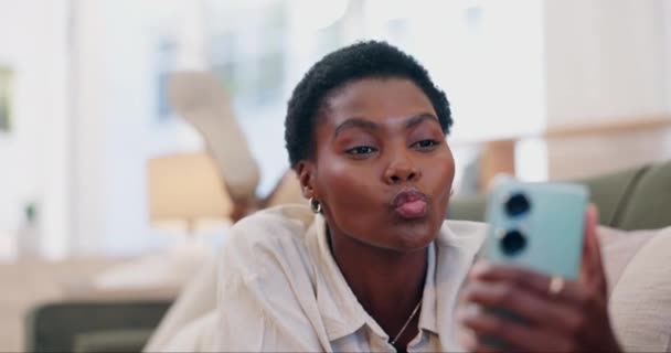 Femme africaine, selfie et baiser sur canapé, sourire et bouder les lèvres avec signe, emoji ou mémoire sur le blog web. Influenceur fille, personne et flux en direct pour l'amour, les médias sociaux ou se détendre sur le canapé-salon dans la maison. - Séquence, vidéo