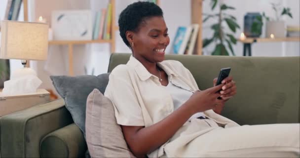 Téléphone, recherche et heureuse femme noire sur un canapé avec une blague sur les médias sociaux, texte ou message drôle dans sa maison. Smartphone, bande dessinée et femme africaine dans un salon avec application pour le streaming vidéo. - Séquence, vidéo
