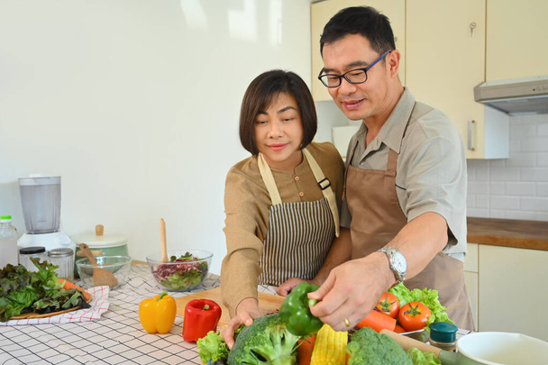 Atraktivní starší pár v neformálních šatech vařící společně v kuchyni. Zdravý životní styl koncept. - Fotografie, Obrázek