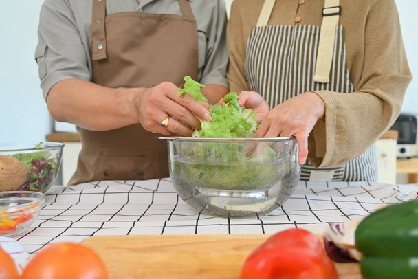 Hände eines Seniorenpaares sortieren frisches Gemüse und bereiten in der Küche einen frischen, gesunden veganen Salat zu. - Foto, Bild
