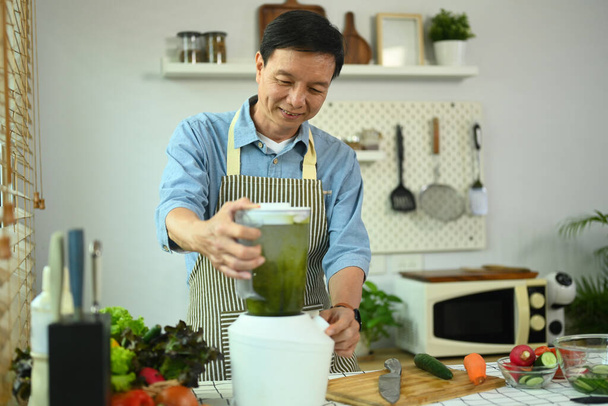 Glücklicher Mann mittleren Alters macht Gemüsesmoothie mit Mixer. Konzept einer gesunden Ernährung. - Foto, Bild