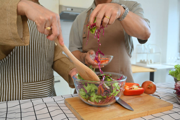 Erschossenes Senioren-Paar kocht gesundes Essen und bereitet Salat in der heimischen Küche zu. - Foto, Bild