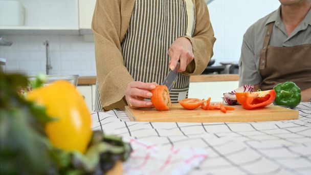 Seniorin schneidet frische Tomaten an Bord und bereitet gesundes Mittagessen in der Küche zu. - Foto, Bild