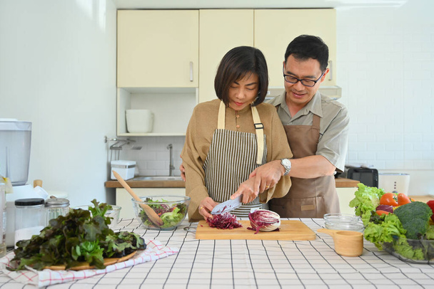 Liebevolles Senioren-Paar hackt in gemütlicher Küche frisches Gemüse für Salat. - Foto, Bild