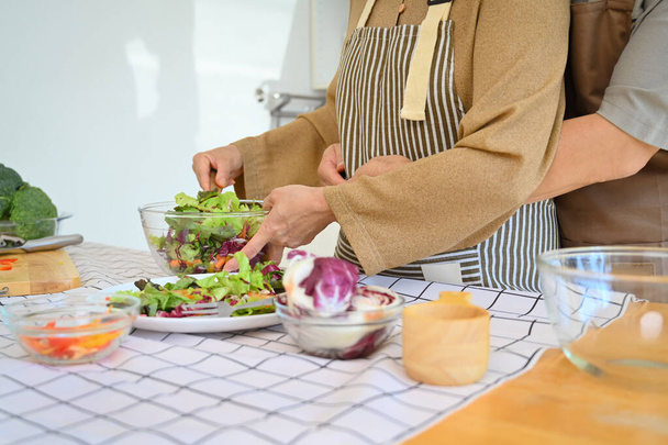 Cropped view of retired couple making fresh organic vegetable salad in kitchen - Photo, Image