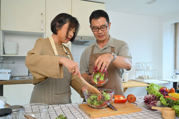 Glückliches asiatisches Rentnerpaar bereitet gesunden vegetarischen Salat mit frischem Bauerngemüse zu. - Foto, Bild