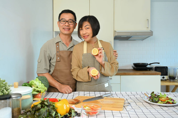 Happy retired couple in aprons cooking healthy food with organic ingredients in kitchen. Healthy lifestyle concept - Photo, Image