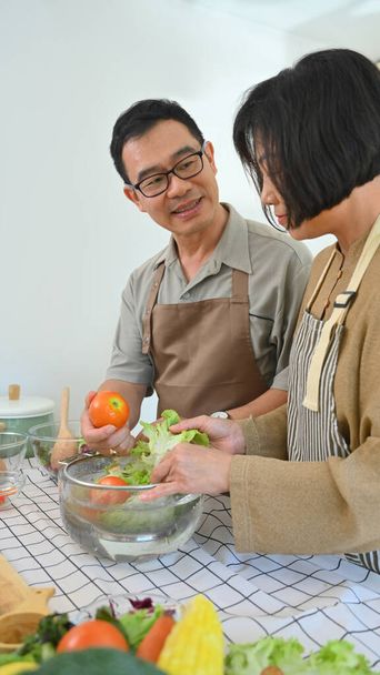 Ευτυχισμένο ζευγάρι ηλικιωμένων έχουν συνομιλία, ενώ το μαγείρεμα υγιεινό γεύμα vegan μαζί στην κουζίνα. - Φωτογραφία, εικόνα