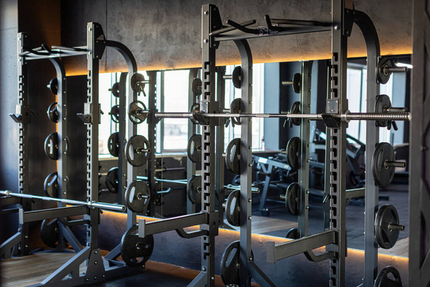 Gym filled with barbells, weights, and various workout gear, creating spot for effective exercises and strength training, surrounded by shadows and focused atmosphere - Photo, Image