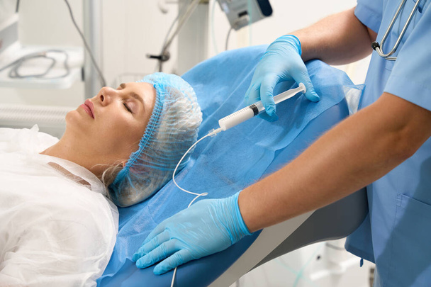 Przycięty obraz lekarza ze strzykawką podczas badania kobiety w ciąży w klinice rozrodczej. Pojęcie ciąży i macierzyństwa - Zdjęcie, obraz