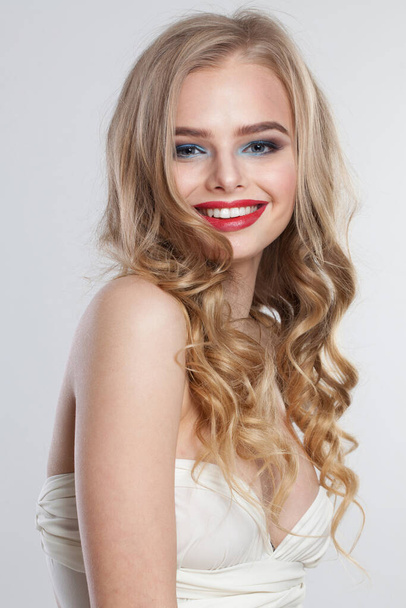 Ευτυχισμένο υγιές ξανθό μοντέλο που στέκεται απομονωμένο σε λευκό φόντο. Γυναίκα με μακιγιάζ, φρέσκο καθαρό δέρμα και κυματιστό ξανθό χτένισμα  - Φωτογραφία, εικόνα