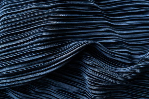 Un tejido plisado de color azul oscuro con una textura brillante y pliegues intrincados. Tiene una sensación artística debido al juego de luz y sombra en los pliegues - Foto, Imagen