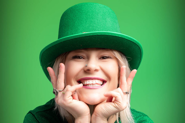 St. Patrick's Day. Fröhliches Mädchen mit Koboldmütze feiert den St. Patrick 's Day in einem grünen Pullover. Festliche Stimmung vor lebendiger grüner Kulisse - Foto, Bild