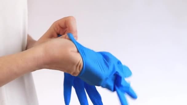 Guanti in nitrile per la pulizia, monouso. Le mani delle donne si mettono guanti azzurri su uno sfondo leggero, una pulizia, un primo piano. Guanti per proteggere le mani da umidità e detergenti - Filmati, video