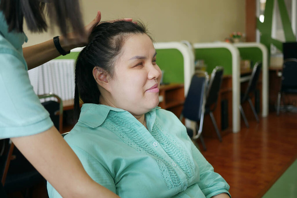 Азіатська жінка людина з сліпотою інвалідністю посміхається щастя, коли її друг робить зачіски для неї на робочому місці.    - Фото, зображення