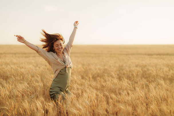 Colta da un'esplosione di gioia, una donna balla liberamente nel campo di grano, la sua figura sagomata contro il soffice bagliore del sole che tramonta - Foto, immagini