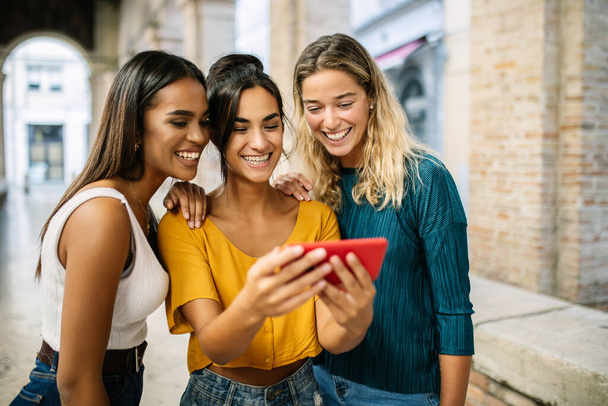 Três jovens mulheres assistindo conteúdo de mídia social no celular na rua da cidade. Estilo de vida de tecnologia e conceito de amizade - Foto, Imagem