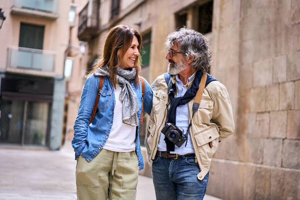 Veselý atraktivní pár seniorů se na sebe usměje na turistické ulici. Důchodci si užívají volný čas společně na dovolené venku. Starší manželský vztah a důchodci dovolená  - Fotografie, Obrázek