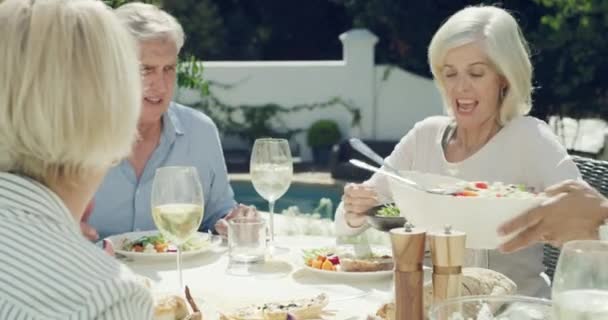 Eten van lunch, senior vrienden en conversatie aan tafel, feesten en feesten in de buitentuin thuis. Eten, wijn en groep mensen die met pensioen gaan bij het verzamelen, alcohol drinken en gelukkig zijn. - Video