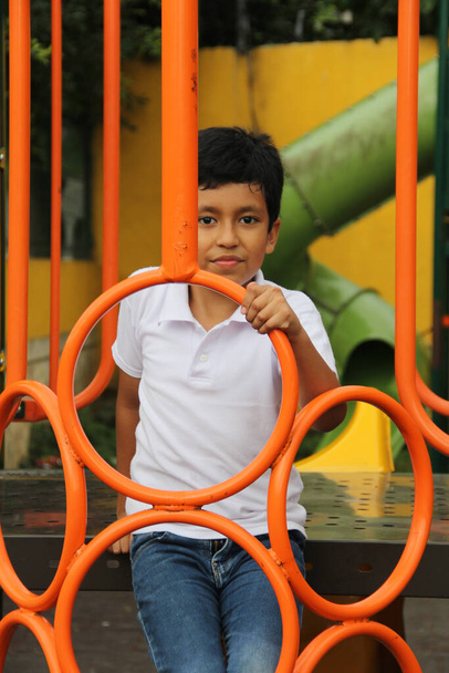 Niño latino de piel oscura de 9 años juega en un patio de recreo como actividad física viviendo en la pobreza como terapia para el TDAH - Foto, Imagen