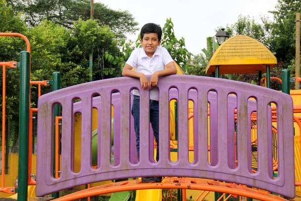Menino latino de 9 anos de idade, de pele escura, joga em um playground como uma atividade física que vive na pobreza como terapia para TDAH - Foto, Imagem