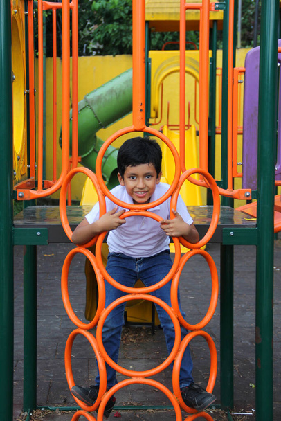 9 yaşındaki esmer tenli Latin çocuk, hiperaktivite terapisi olarak yoksulluk içinde yaşayan fiziksel bir aktivite olarak oyun bahçesinde oynuyor. - Fotoğraf, Görsel
