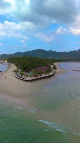 Um par de homens e mulheres caminhando na praia em Koh Muk uma ilha tropical com palmeiras e areia branca macia, e um turqouse colorido oceano em Koh Mook Andaman Sea em Trang Tailândia - Filmagem, Vídeo