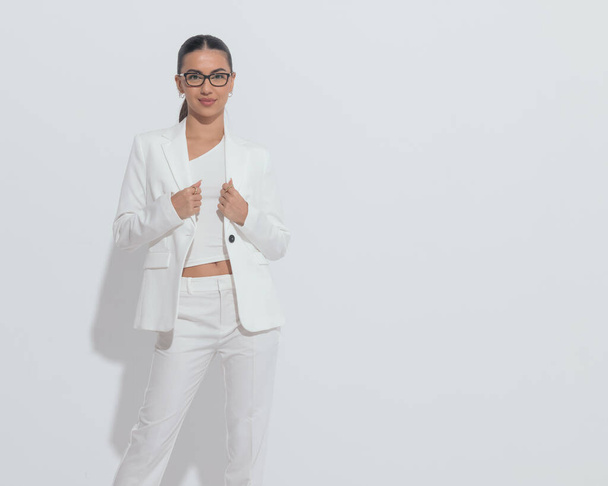 ritratto di bella giovane donna d'affari con occhiali di regolazione vestito e sorridente mentre in piedi e in posa di fronte a sfondo grigio  - Foto, immagini