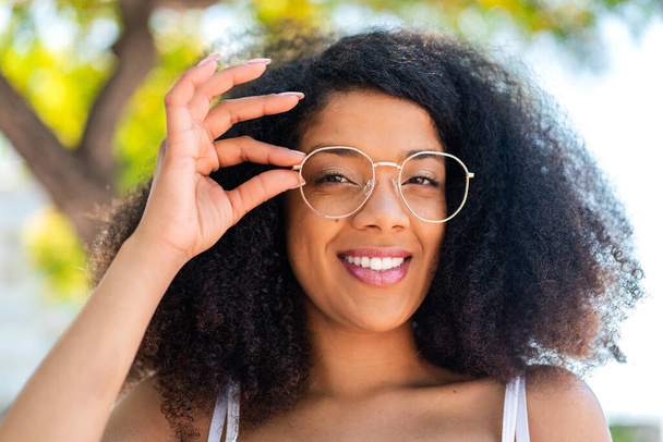 Fiatal afro-amerikai nő a szabadban, szemüveggel és boldog arckifejezéssel. - Fotó, kép