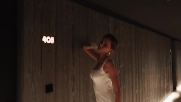 Ένα μοντέλο μόδας θέτει σε ένα λευκό φόρεμα στο διάδρομο στο φως της κάμερας. Έννοια της μόδας γυρίσματα. Μεγάλη επίδραση έκθεσης του πλαισίου. 4K - Πλάνα, βίντεο