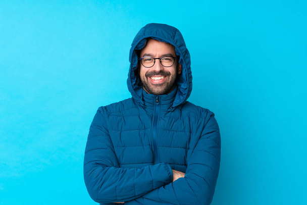 Muž nosí zimní bundu a drží odnést kávu přes izolované modré pozadí s brýlemi a šťastný - Fotografie, Obrázek