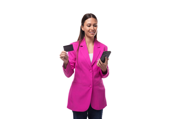 junge gepflegte lächelnde Brünette erfolgreiche Chefin Frau in rosa Jacke verwendet eine Kreditkarte online. - Foto, Bild