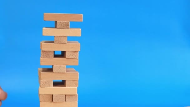A woman plays Jenga on a blue bright background. The concept of family vacation, holidays, entertainment. A woman's hand takes out a block from a wooden toy tower. Game - Footage, Video